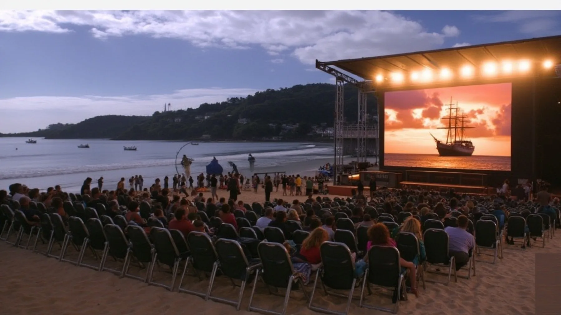 Tela de cinema montada na praia ao entardecer